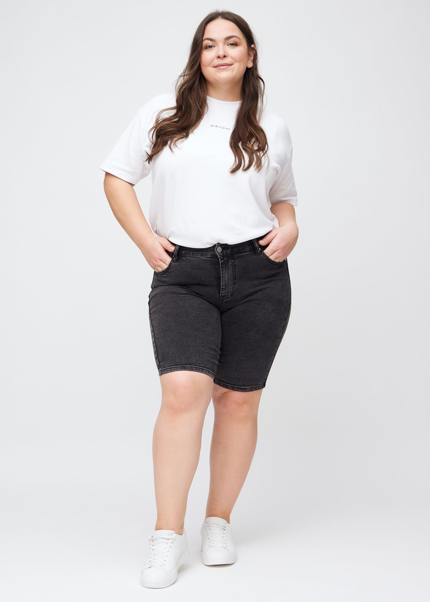 Fuldt billede af en plus-size model i mørkegrå denim skinny middle shorts.