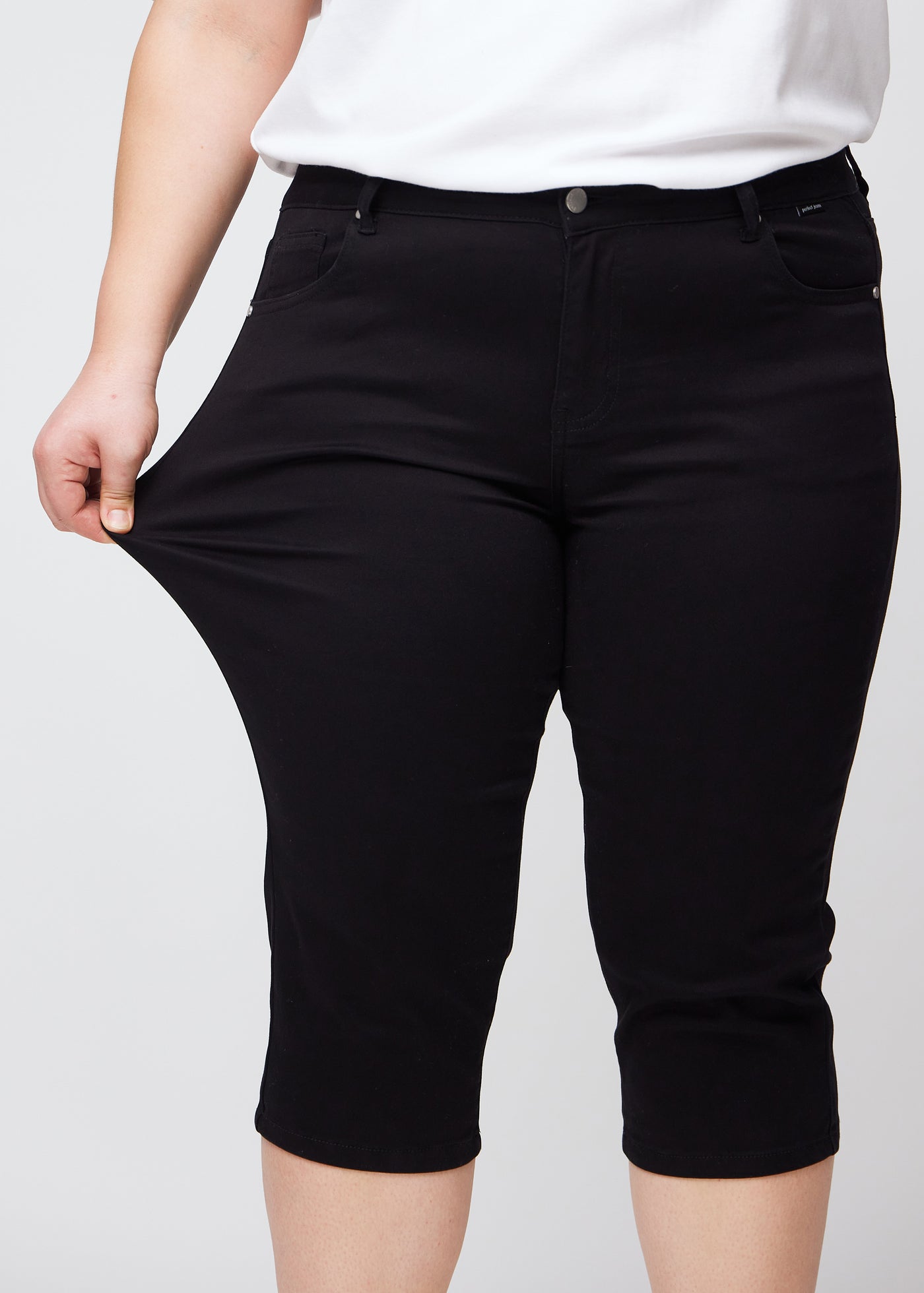 Plus-size model viser stretch ved at trække i caprisene ved låret – fokus på komfort og fleksibilitet.