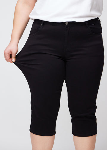 Plus-size model viser stretch ved at trække i caprisene ved låret – fokus på komfort og fleksibilitet.