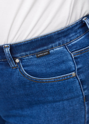 Detaljebillede af forlommen på de mørkeblå denim slim capris i farven Oceans – logo og snit fremhævet på plus-size model.