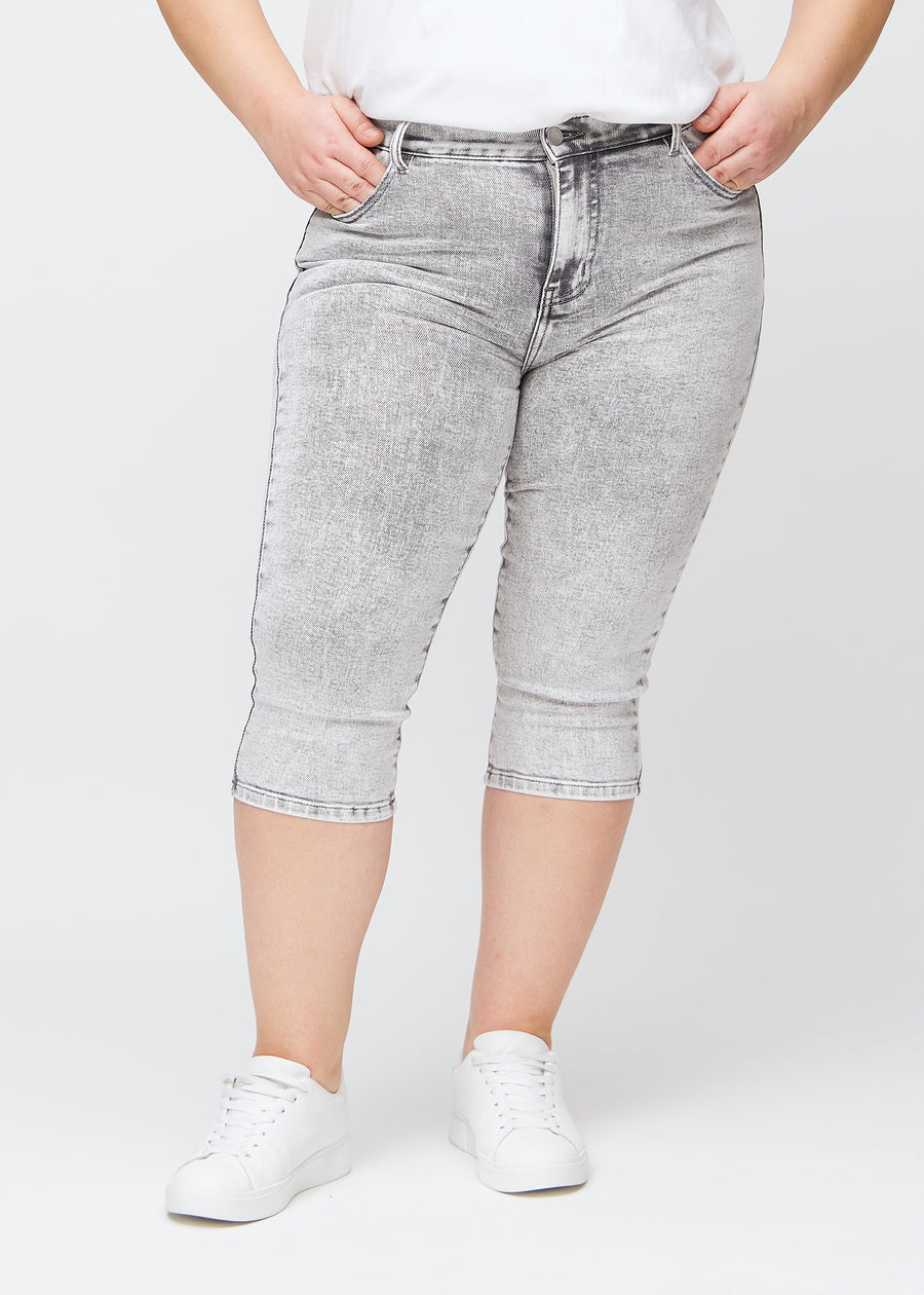 Lysegrå denim skinny capris, modelnavn Ashes, som sidder tæt til benet og slutter lige under knæet på en plus-size model, set forfra.