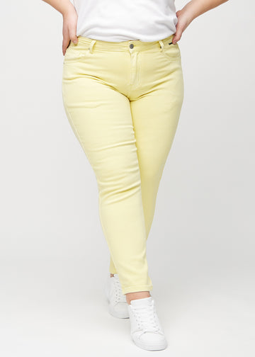 Lysegule slim jeans, modelnavn Lemonades, som sidder tæt til benet, dog lidt løsere ved anklen, på en plus-size model, set forfra.