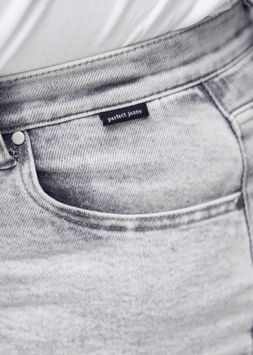 Nærbillede af lysegrå denim med Perfect Jeans logoetiket ved forlommekanten, på en plus-size model.