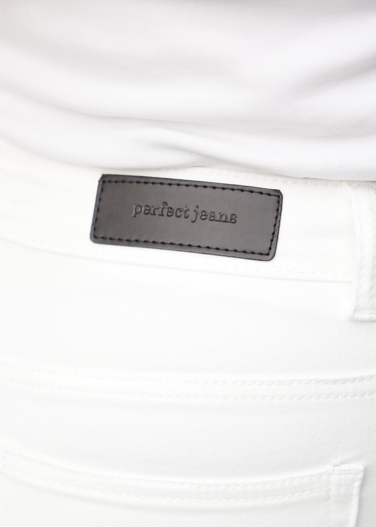 Nærbillede af hvidt jeansmateriale med Perfect Jeans læderpatch bagpå i taljen, på en plus-size model.