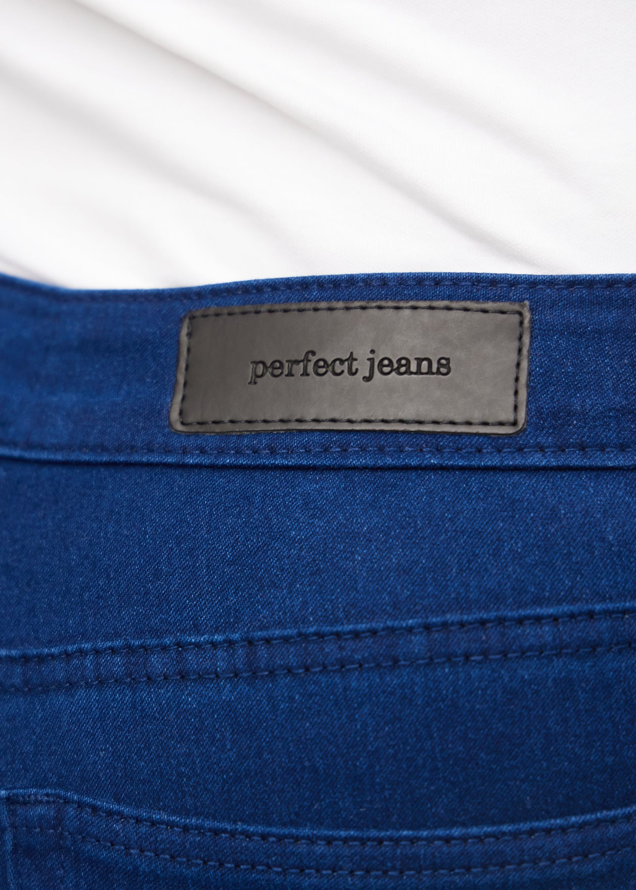Nærbillede af mørkeblåt jeansmateriale med Perfect Jeans læderpatch bagpå i taljen, på en plus-size model.