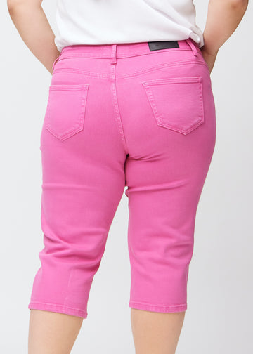 Tæt billede af bagdelen på en plus-size model i lyserøde slim capris – detaljefokus på lommer og syninger.