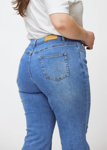 Blaue Mid-Rise-Bootcut-Jeans in der Farbe Rivers. Nahaufnahme der Rückseite an einem Plus-Size-Model, um Details zu zeigen.