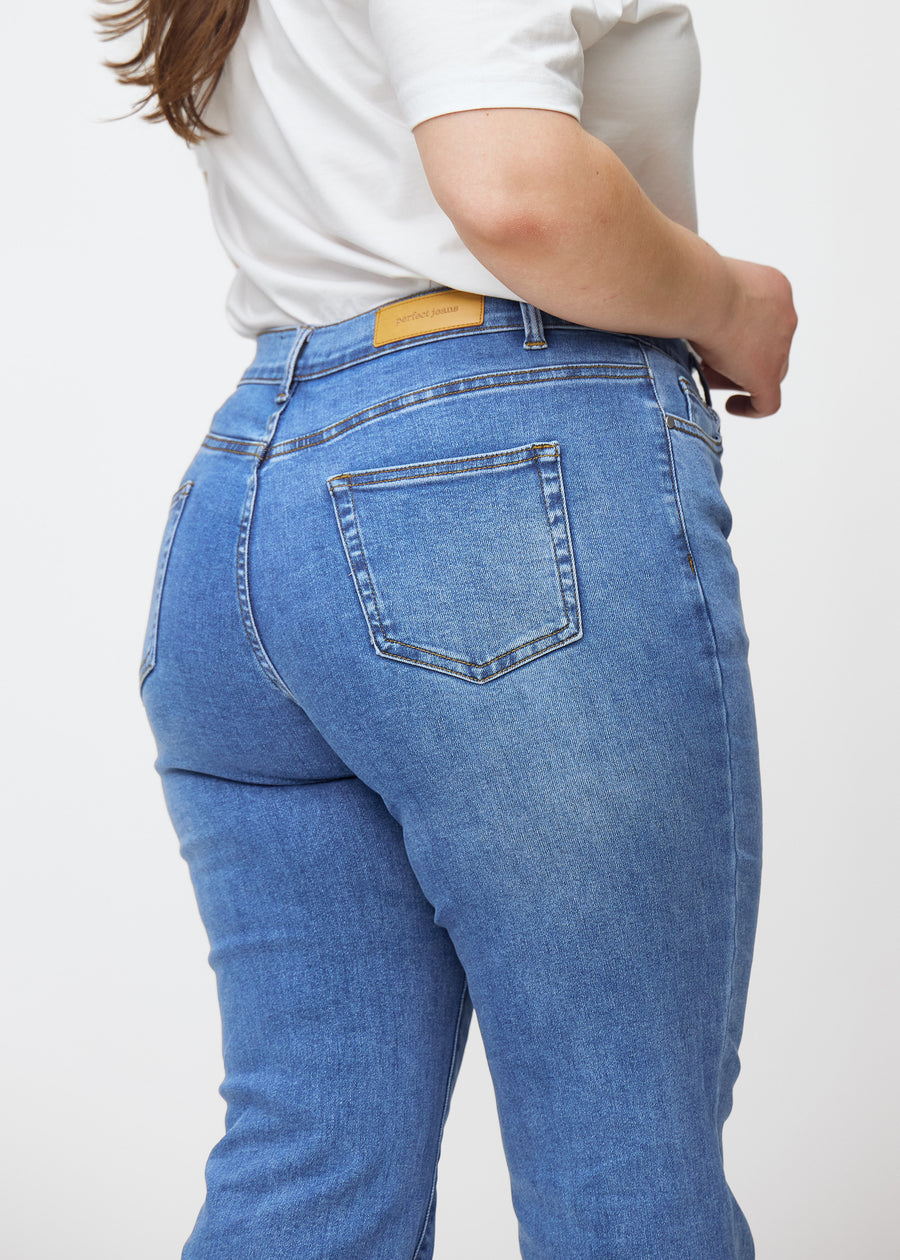 Blaue Mid-Rise-Bootcut-Jeans in der Farbe Rivers. Nahaufnahme der Rückseite an einem Plus-Size-Model, um Details zu zeigen.