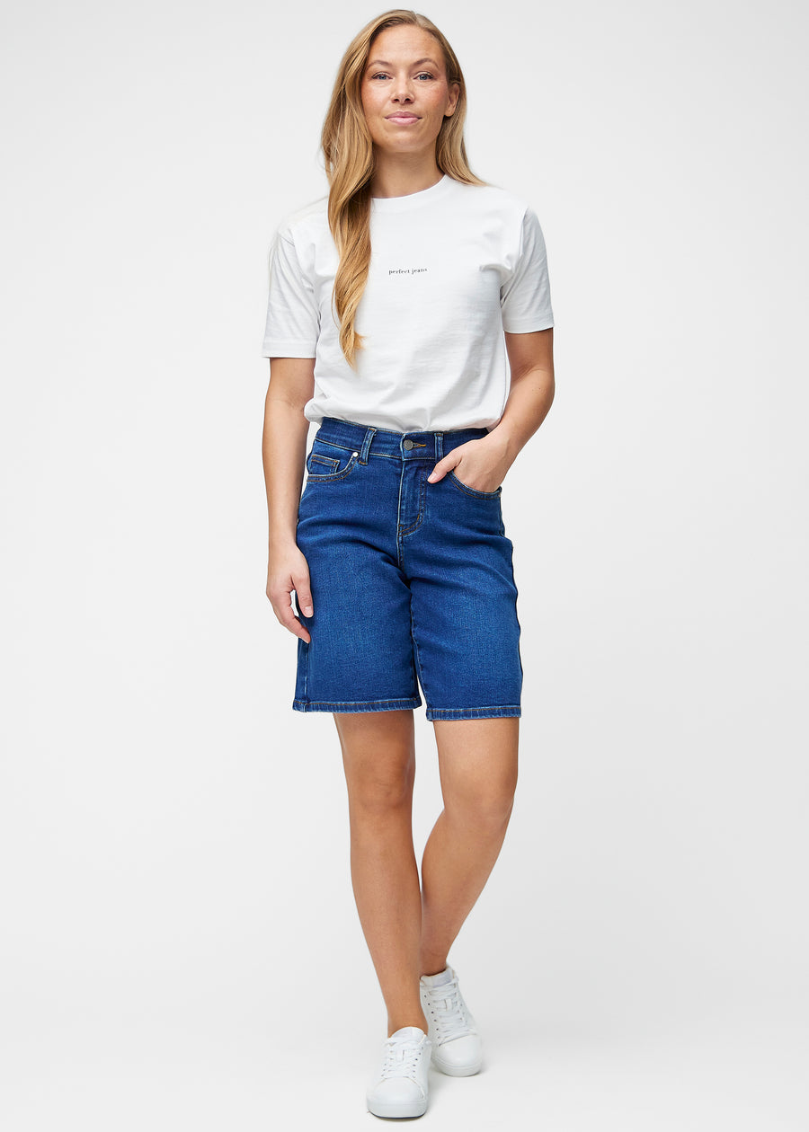 Fuldt billede af model i løse, mørkeblå denim shorts i farven Oceans, der går til lige over knæet.