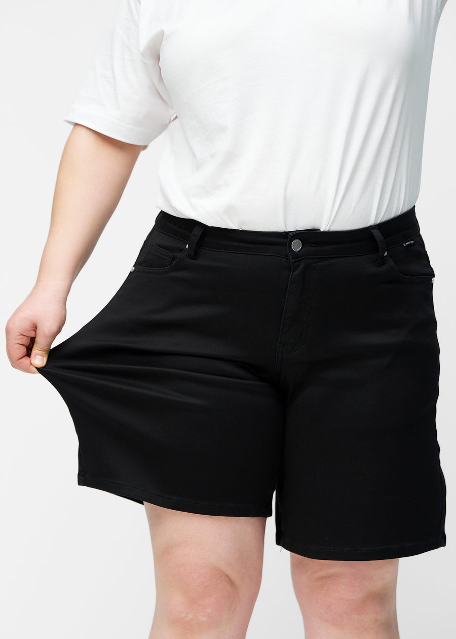 Plus-size model strækker de løse, sorte shorts i farven Ravens ved hoften for at vise materialets stretch.