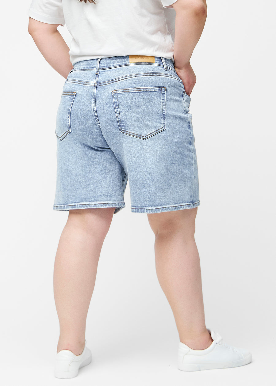 Lockere, hellblaue Denim-Shorts in der Farbe Waves von hinten am Plus-Size-Model, sodass Passform und Länge sichtbar sind.