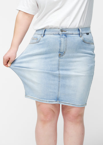 Plus-size model strækker lyseblå, tætsiddende og knælang denimnederdel ved låret for at vise stretch.