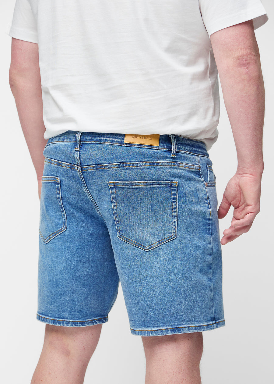 Blaue Denim-Shorts für Herren in der Farbe Rivers von hinten am Plus-Size-Modell gesehen, sodass die Länge bis knapp über das Knie sichtbar ist.