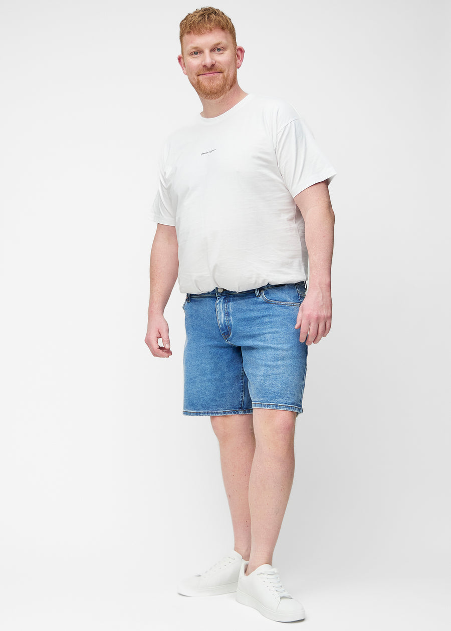 Ganzkörperbild eines Plus-Size-Modells in blauen Denim-Shorts für Herren in der Farbe Rivers mit Regular-Passform.
