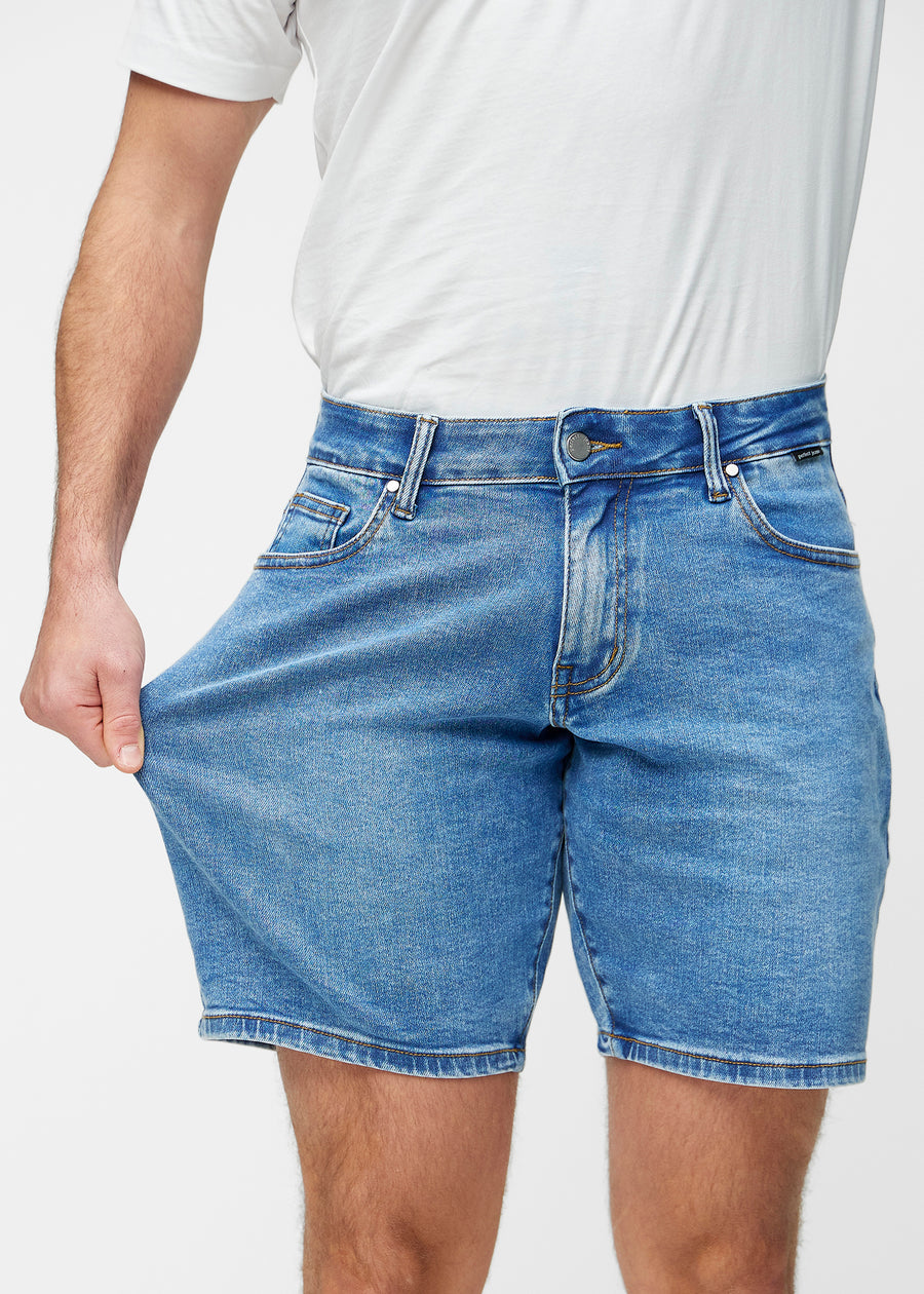 Modell dehnt blaue Denim-Shorts für Herren in der Farbe Rivers am Oberschenkel, um den Stretch des Materials zu zeigen.