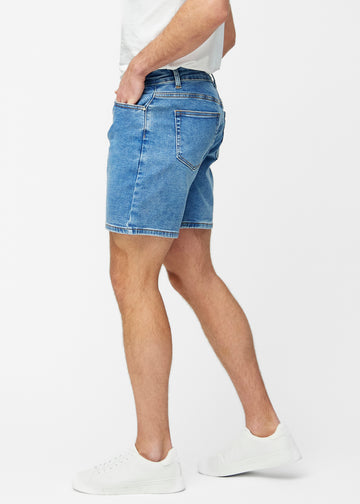 Modell dehnt blaue Denim-Shorts für Herren in der Farbe Rivers am Oberschenkel, um den Stretch des Materials zu zeigen.