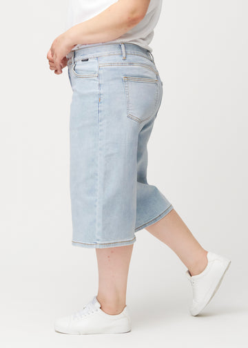 Lockere, hellblaue Waves Denim-Capris an einem Plus-Size-Model von der Seite, die den weiten Schnitt und die Länge bis knapp unter das Knie zeigen.