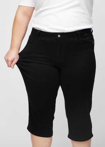 Ein Plus-Size-Model zieht die Capris am Oberschenkel, um den Stretch zu zeigen.