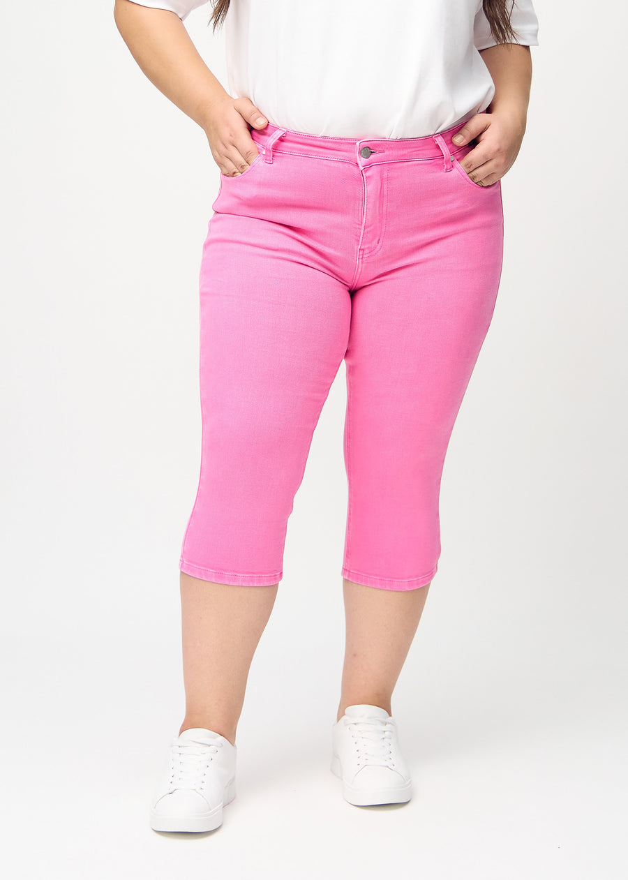 Skinny-Capris für Damen in pastellrosa Jeansstoff, Farbe Flamingos. Vorderansicht an einem Plus-Size-Model, eng geschnitten bis knapp unter das Knie.
