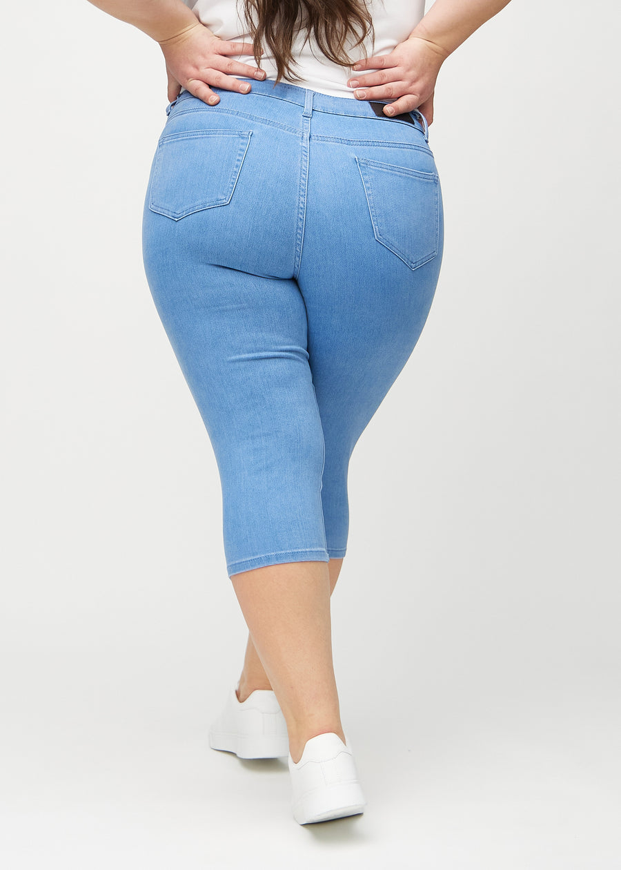 Skinny-Capris für Damen in blauem Jeansstoff, Farbe Geraniums. Rückansicht an einem Plus-Size-Model, zeigt die Passform und Gesäßtaschen.