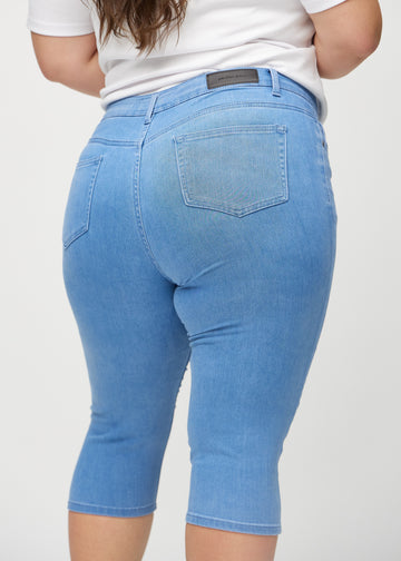 Skinny-Capris für Damen in blauem Jeansstoff, Farbe Geraniums. Nahaufnahme von hinten an einem Plus-Size-Model, zeigt Taschen und Nähte.