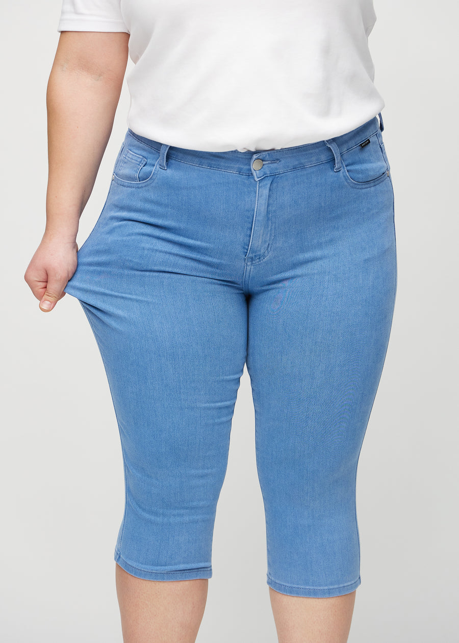 Skinny-Capris für Damen in blauem Jeansstoff, Farbe Geraniums. Ein Plus-Size-Model dehnt den Stoff, um den Stretch zu zeigen.