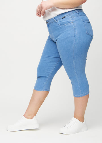 Skinny-Capris für Damen in blauem Jeansstoff, Farbe Geraniums. Seitenansicht an einem Plus-Size-Model, die figurbetonte Passform ist zu sehen.
