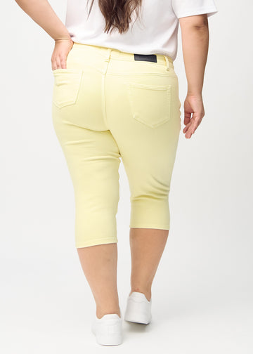 Hellgelbe skinny Capris, von hinten gesehen, an einem Plus-Size-Model, sodass das gesamte Produkt zu sehen ist.