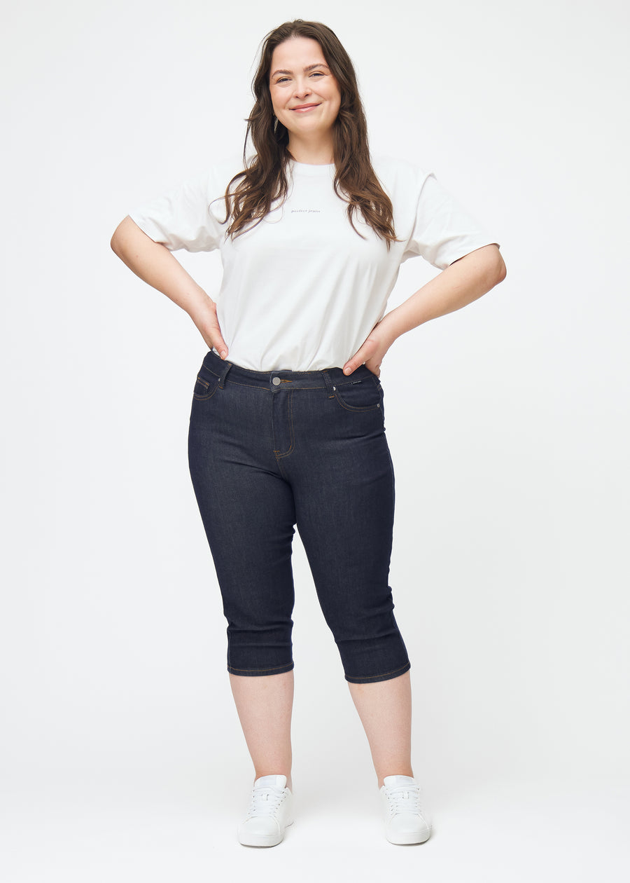 Ganzkörperbild eines Plus-Size-Models in tief dunkelblauen Denim-Capris für Damen in der Farbe Midnights mit Skinny-Passform.