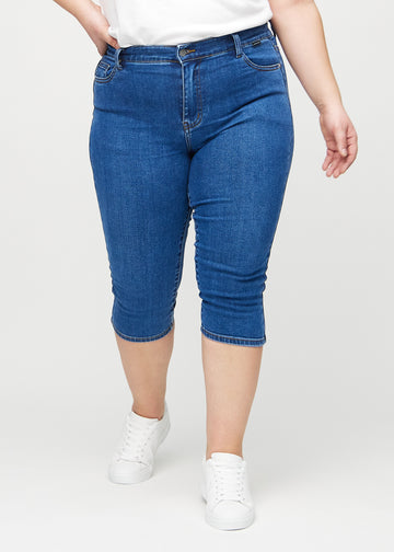 Dunkle Denim-skinny-Capris, Modellname Oceans, die eng am Bein anliegen und knapp unter dem Knie enden, an einem Plus-Size-Model von vorne gesehen.