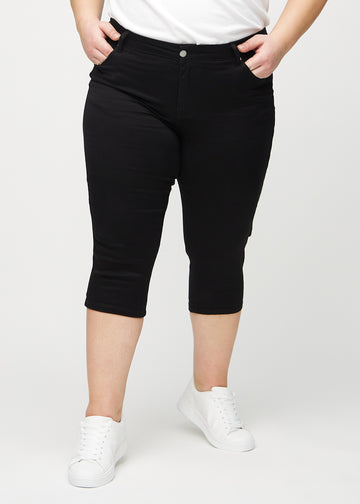 Schwarze skinny Capris, Modellname Ravens, die eng am Bein anliegen und direkt unter dem Knie enden, an einem Plus-Size-Model von vorne gesehen.