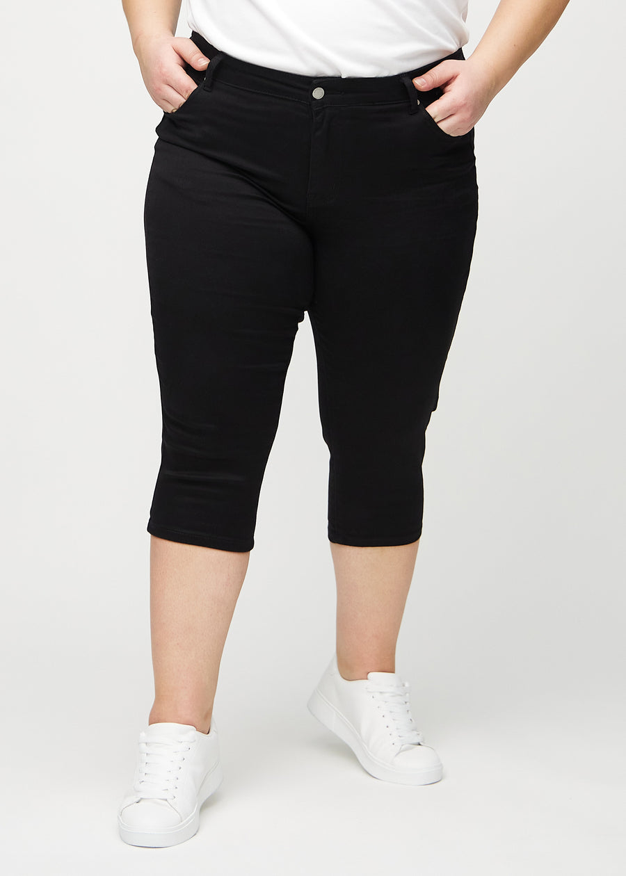 Schwarze skinny Capris, Modellname Ravens, die eng am Bein anliegen und direkt unter dem Knie enden, an einem Plus-Size-Model von vorne gesehen.