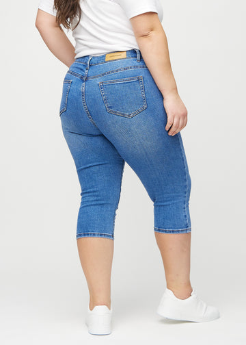 Skinny-Capris für Damen in blauem Denim, Farbe Rivers. Rückansicht an einem Plus-Size-Model, zeigt die Passform und Gesäßtaschen.