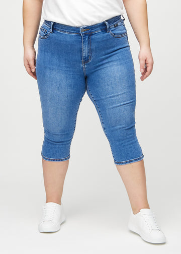 Skinny-Capris für Damen in blauem Denim, Farbe Rivers. Vorderansicht an einem Plus-Size-Model, eng geschnitten bis knapp unter das Knie.