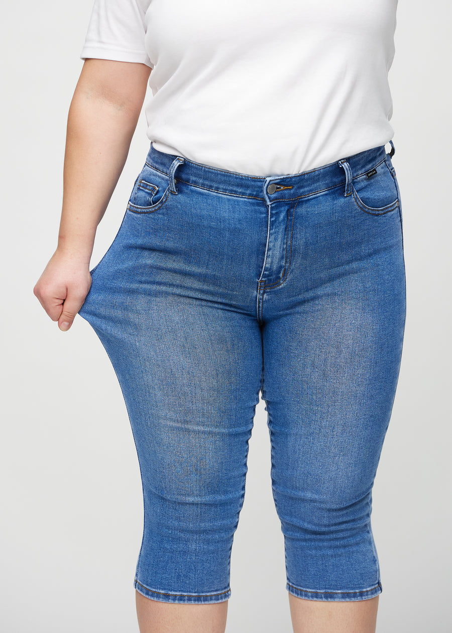 Skinny-Capris für Damen in blauem Denim, Farbe Rivers. Ein Plus-Size-Model dehnt den Stoff, um den Stretch zu zeigen.