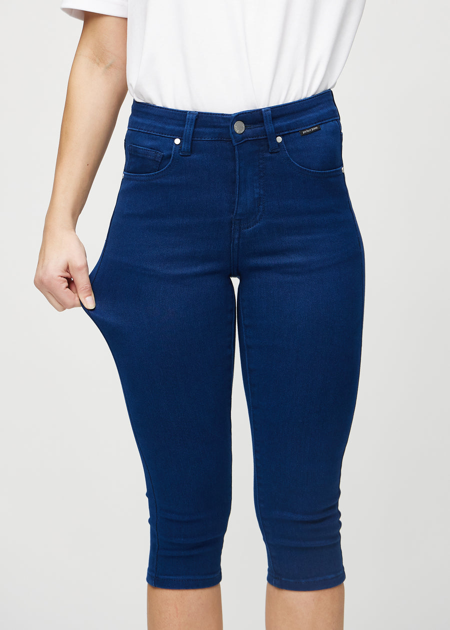 Skinny-Capris für Damen in dunkelblauem Jeansstoff, Farbe Royals. Ein Model dehnt den Stoff, um den Stretch zu zeigen.