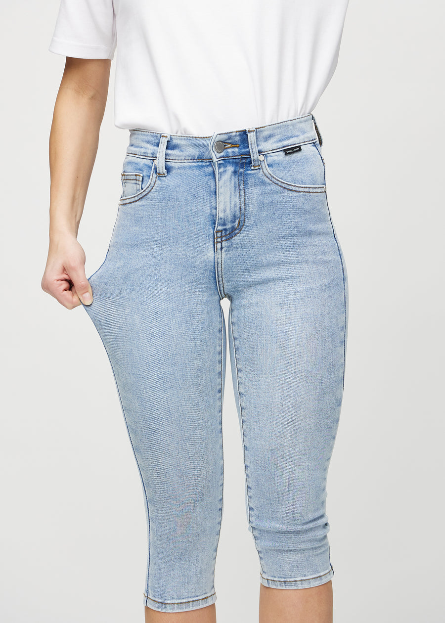Skinny-Capris für Damen in hellblauem Denim, Farbe Waves. Ein Model dehnt den Stoff, um den Stretch zu zeigen.