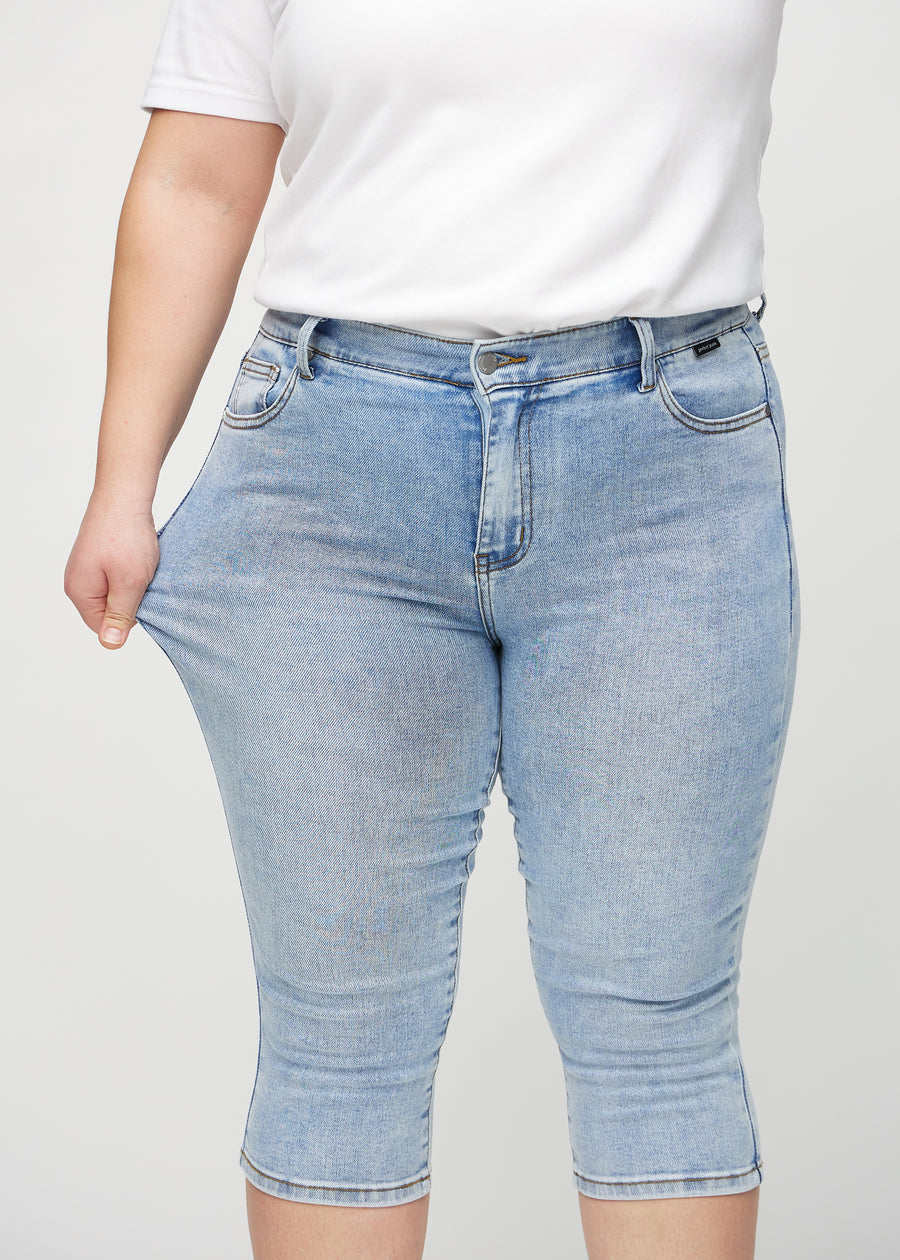 Skinny-Capris für Damen in hellblauem Denim, Farbe Waves. Ein Plus-Size-Model dehnt den Stoff, um den Stretch zu zeigen.