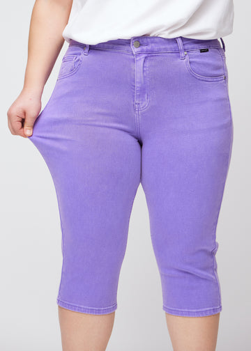Slim-Capris für Damen aus pastellviolettem Jeansstoff, Farbe Lavenders. Ein Plus-Size-Model dehnt den Stoff am Oberschenkel, um die Flexibilität zu zeigen.