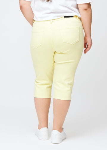 Hellgelbe slim Capris von hinten an einem Plus-Size-Model gesehen, deutliches Bild des gesamten Produkts und der Taschen.