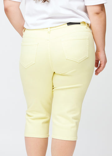 Nahes Bild der Rückseite eines Plus-Size-Models in hellgelben slim Capris, Fokus auf Details an Taschen und Nähten.