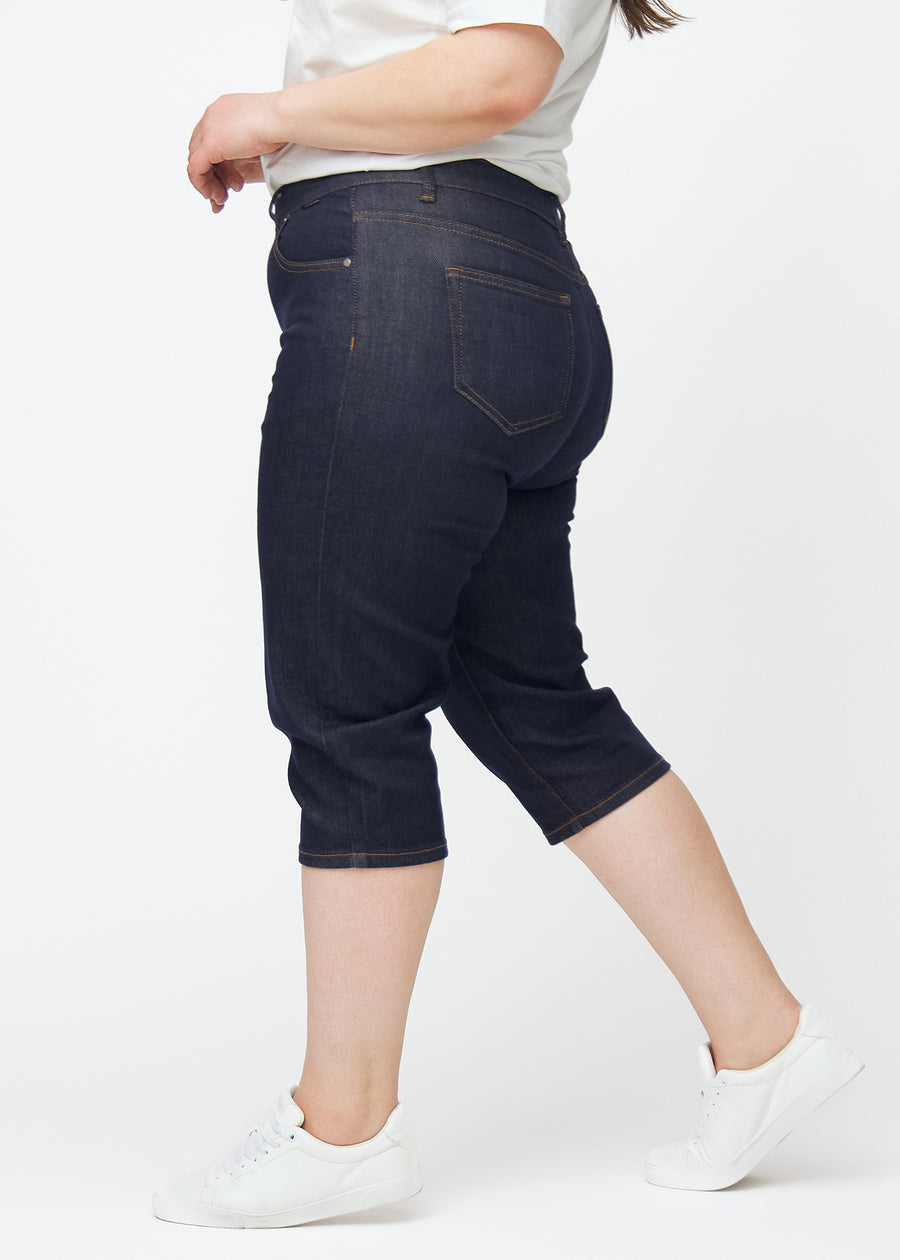 Tief dunkelblaue Denim-Capris für Damen in der Farbe Midnights mit Slim-Passform, von der Seite auf einem Plus-Size-Model gesehen.