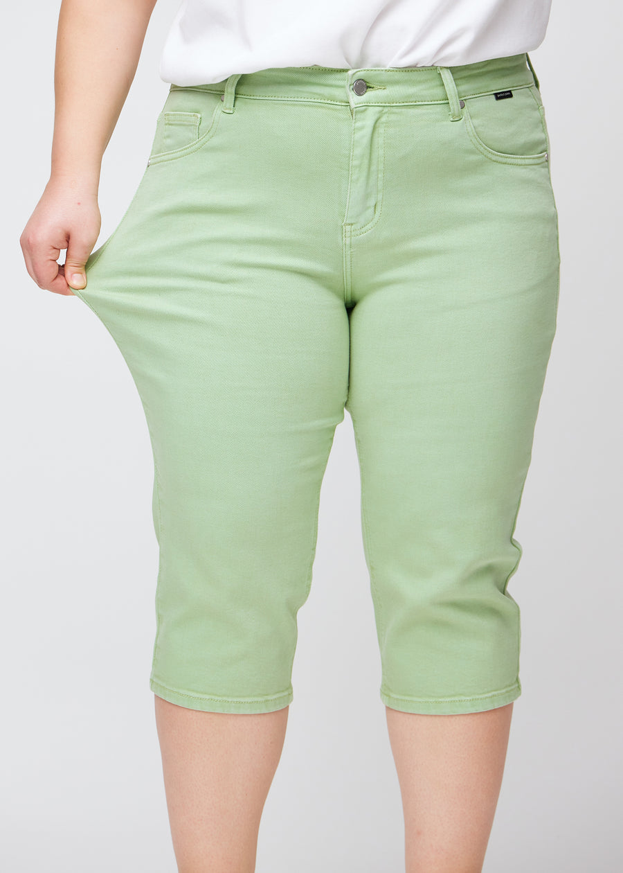 Ein Plus-Size-Model zeigt den Stretch, indem es die Capris am Oberschenkel auseinanderzieht, Fokus auf Komfort und Flexibilität.
