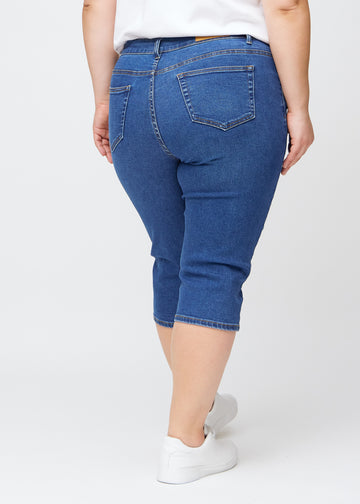 Slim-Capris für Damen aus dunkelblauem Denim, Farbe Oceans. Rückansicht an einem Plus-Size-Model, zeigt Passform, Länge und Gesäßtaschen.