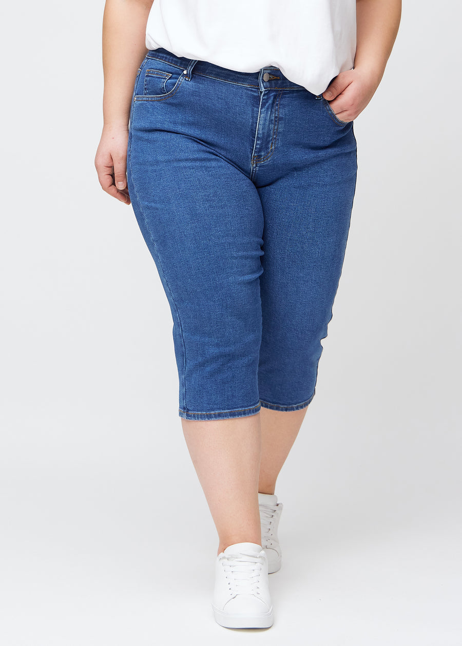 Slim-Capris für Damen aus dunkelblauem Denim, Farbe Oceans. Vorderansicht an einem Plus-Size-Model, figurbetonter Schnitt bis knapp unter das Knie.