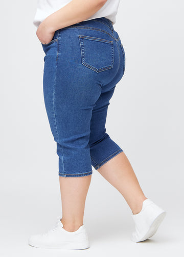 Slim-Capris für Damen aus dunkelblauem Denim, Farbe Oceans. Seitenansicht an einem Plus-Size-Model, figurbetonter Schnitt und mittelhoher Bund (Mid Rise).