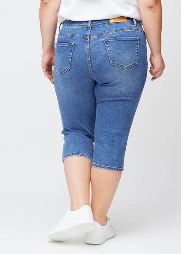 Slim-Capris für Damen aus blauem Denim, Farbe Rivers. Rückansicht an einem Plus-Size-Model, zeigt Passform, Länge und Gesäßtaschen.