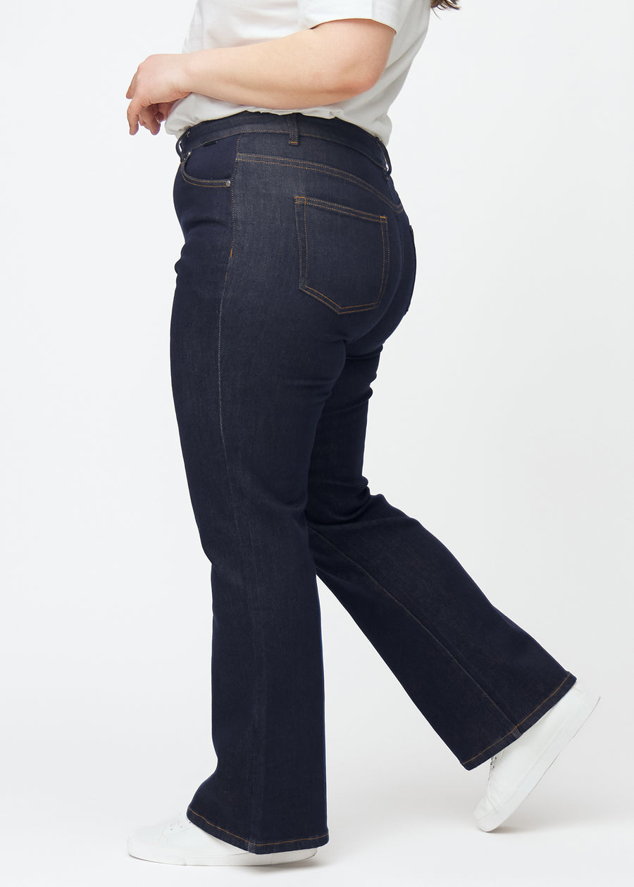 Tief dunkelblaue Denim jeans für Damen in der Farbe Midnights mit Bootcut-Passform, seitlich an einem Plus-Size-Model gezeigt.