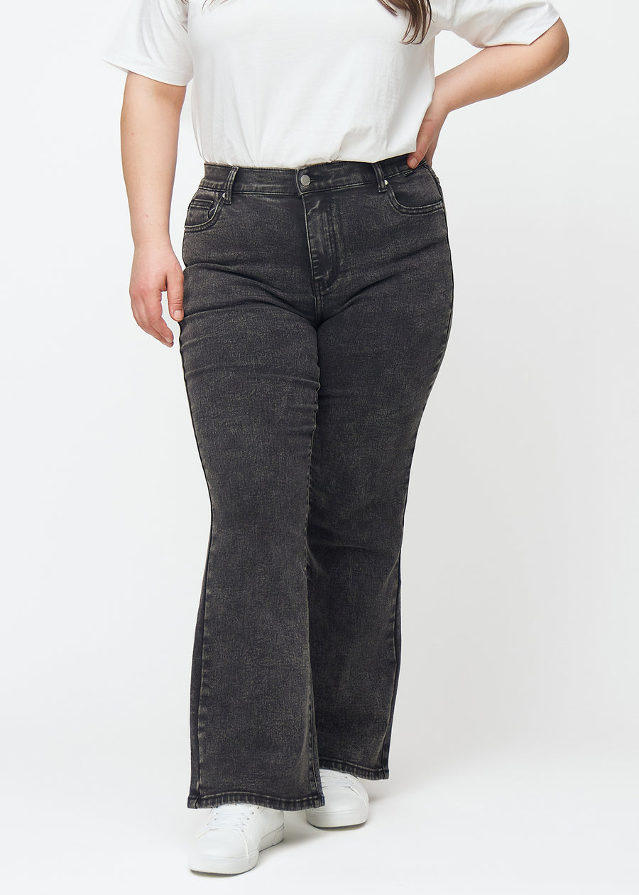 Dunkelgraue Mid-Rise-Bootcut-Jeans in der Farbe Shadows. Vorderansicht an einem Plus-Size-Model, an Hüfte und Oberschenkeln anliegend mit leicht ausgestelltem Bein.