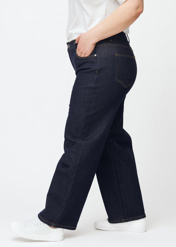 Tief dunkelblaue Denim jeans für Damen in der Farbe Midnights mit loose Passform, von der Seite an einem Plus-Size-Model gezeigt.

